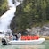 A tour group donned in waterproof suits watch a rushing waterfall as they sit in a stopped rigid inflatable boat